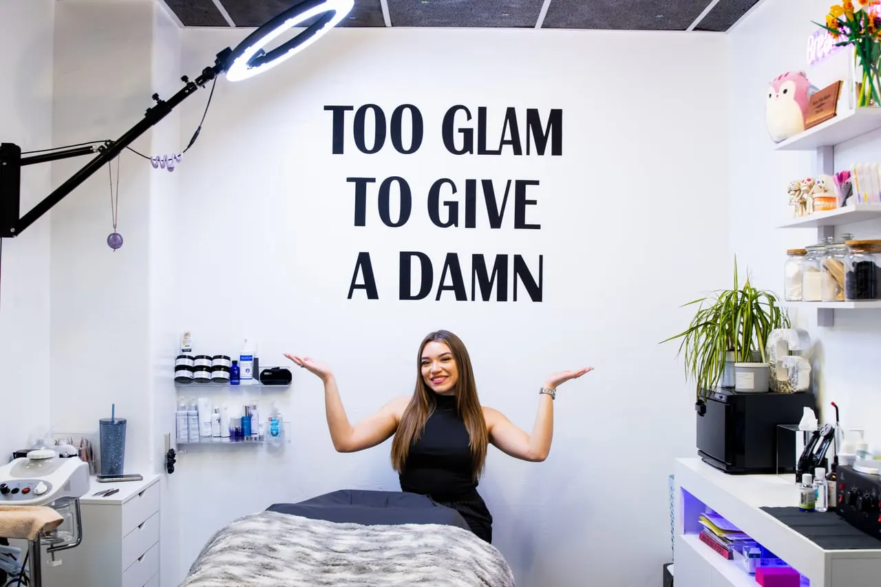 Gabriela in the GLAMSTHETICS SLC treatment room under the "Too Glam to Give a Damn" wall